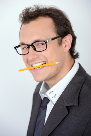 Creative and playful businessman. Playful young man in formalwear holding a pencil and looking at camera while standing against grey backgroundの写真素材
