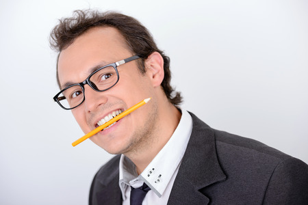 Creative and playful businessman. Playful young man in formalwear holding a pencil and looking at camera while standing against grey backgroundの写真素材