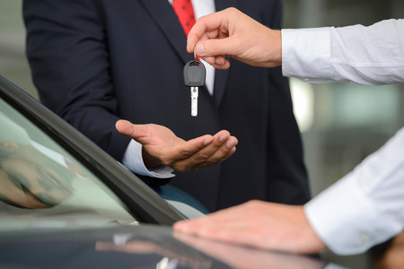 Giving a key of a brand new car. Handsome young classic car salesman giving a car key to the owner and smilingの写真素材