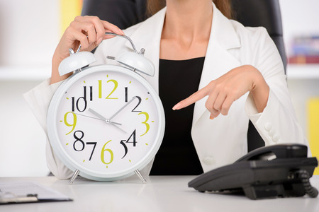 Attractive businesswoman showing white clock in officeの写真素材