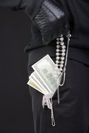 Criminal in a balaclava holding a fistful of money conceptual of the loot from a robbery bribe corruption coercion payoff ransom or mob protection moneyの写真素材