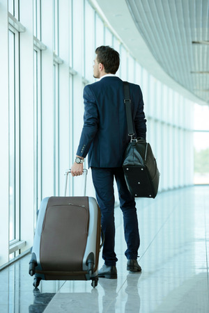 Business traveler pulling suitcase and holding passport and airline ticketの写真素材