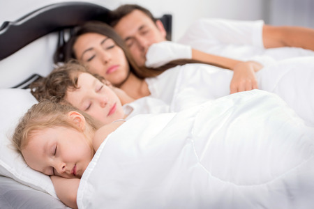 Young family of Dad, mom, little boy and little girl sleeping in bed in bedroom at homeの写真素材