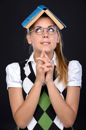 Young nerd woman crazy expression in glasses, holding book on head on black backgroundの写真素材
