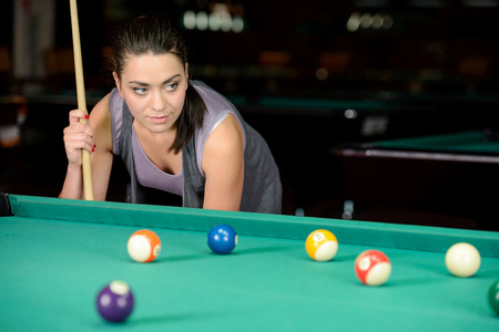 Young woman playing billiards in the dark billiard clubの写真素材