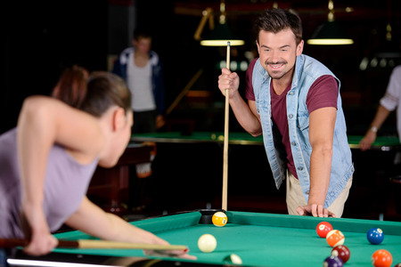 Young couple plays billiards in the dark billiard club