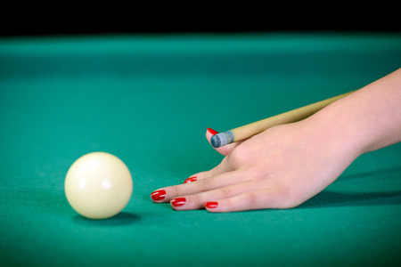 Billiards. Billiard balls on green table and white ball on the foreground. Hand of someone who is...