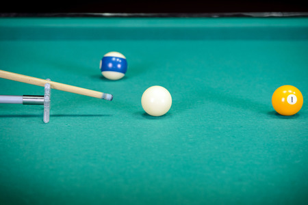 Billiards. Billiard balls on green table and white ball on the foreground. Hand of someone who is...