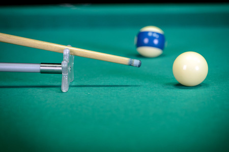 Billiards. Billiard balls on green table and white ball on the foreground. Hand of someone who is...