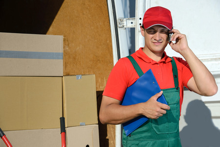 Smiling young male postal delivery courier man in front of cargo van delivering boxesの写真素材