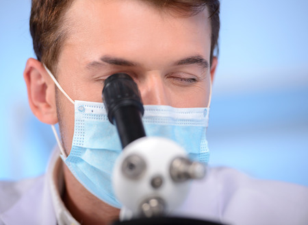 Serious clinician studying chemical element in laboratory using a microscope
