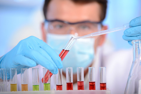 Portrait of a chemist holding a tube with liquid. Investigator checking test tubes. Man wears...