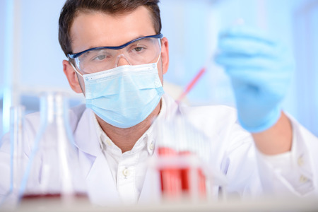 Portrait of a chemist holding a tube with liquid. Investigator checking test tubes. Man wears...