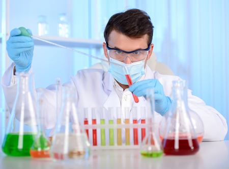 Portrait of a chemist holding a tube with liquid. Investigator checking test tubes. Man wears...