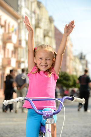 Beautiful smiling little girl riding a bike on the street in cityの写真素材