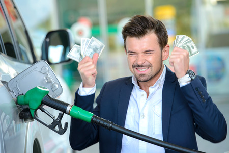 Emotional businessman counting money with gasoline refueling car at fuel stationの写真素材