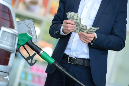 Businessman counting money with gasoline refueling car at fuel stationの写真素材