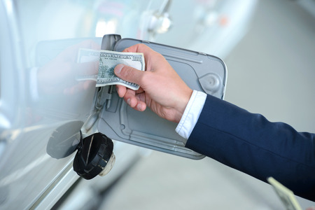 Hand of businessman that puts money into the tank of his car instead of gasoline at filling stations. Concept of expensive fuelの写真素材