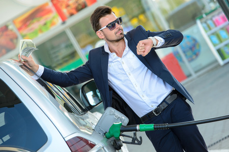 Young businessman refueling car tank at fuel stationの写真素材