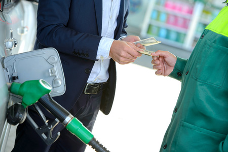 Businessman give money dispensers, filled car on gas stationの写真素材