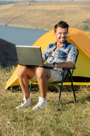 Portrait of succesful man with laptop sitting in folding chair near camp tent outdoorsの写真素材