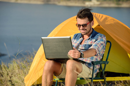 Portrait of succesful man with laptop sitting in folding chair near camp tent outdoorsの写真素材