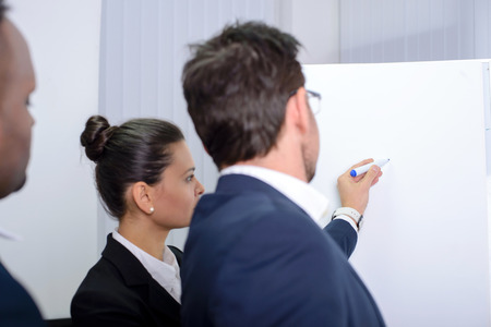 Young multiethnic business team planning a new strategy standing grouped in front of a flip chart analyzing a chartの写真素材