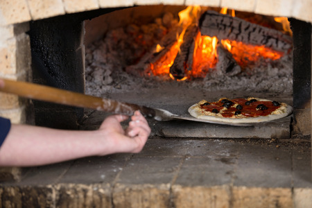Close-up. Chef inserts the pizza inside the wood oven to bake.