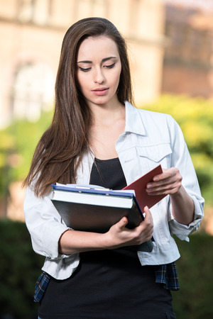 Portrait of a young beautiful student with university building in the background. She is holding books in hands.の写真素材