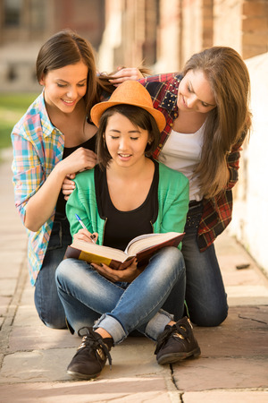 Portrait of young smart female students with university building in the background. Girls are looking in a book.の写真素材