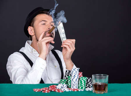 Wealthy man is playing poker in casino. With hat, cigar and a glass of whiskey.の写真素材
