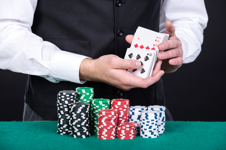Close-up of a croupier's hands with cards and gambling chips on the green table and.