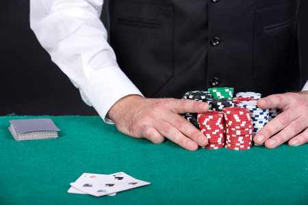 Close-up of a croupiers hand is holding gambling chips on table.