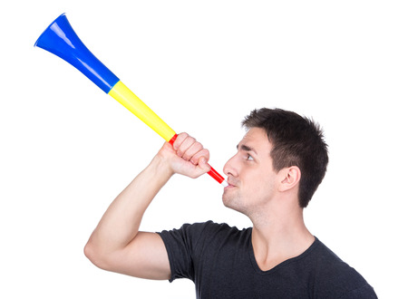 Portrait of football fan is blowing by vuvuzela, isolated on white.の写真素材