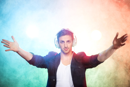 Portrait of a young dj with headphones on the foggy background.