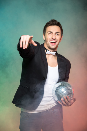 Portrait of young handsome man with mirror ball on a color background and fog.の写真素材