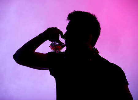 Silhouette of a young man who drinks alcohol on a colored background.の写真素材