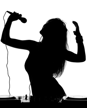 Beautiful busty DJ with her headphones, microphone is standing at her deck mixing sound.の写真素材