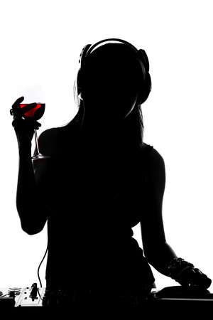Beautiful male DJ with a glass if wine, headphones is standing at her deck mixing sound.の写真素材