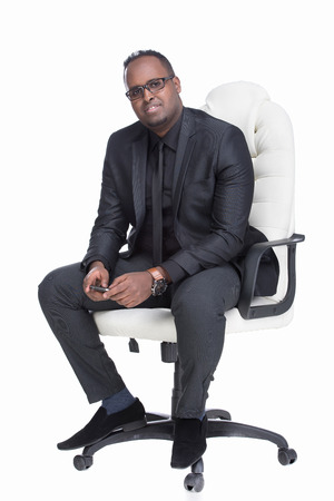 Portrait of young black man is sitting at the chair, on white background.の写真素材