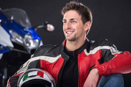 Portrait of young smiling man with helmet. The motorcycle is on black background.