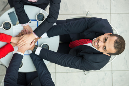 Top view of young man at business meeting, while business team are showing unity with their hands...