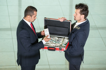 Two business men with metal suitcase full of money.