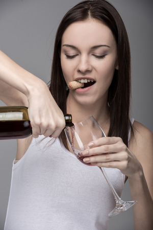 Young woman pours wine into a glass. Concept of bad habits.の写真素材