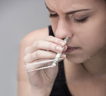 Addicted young woman is sniffing lines of drugs.
