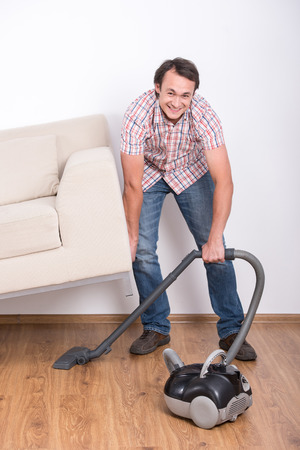 Young smiling man is doing house cleaning with vacuum.の写真素材