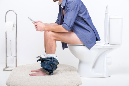 Businessman is working with digital tablet while sitting on the toilet.の写真素材