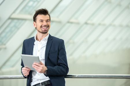 Happy young business man with tablet at work in modern office.