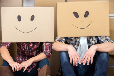 Couple with cardboard boxes on their heads with smiley face are sitting on floor after the moving house.の写真素材