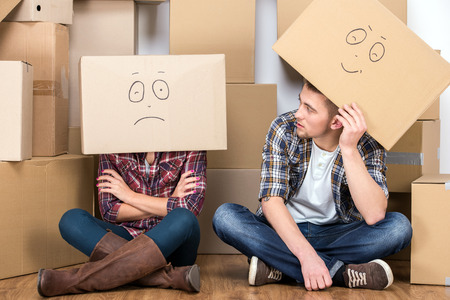 Couple with cardboard boxes on their heads with smiley face are sitting on floor after the moving house.の写真素材